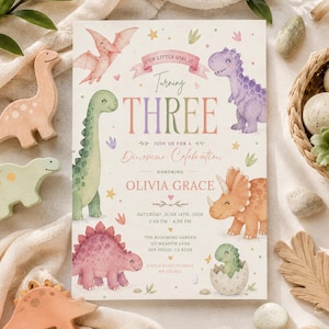 Peut inclure: Une carte d'invitation rectangulaire avec des illustrations à l'aquarelle de dinosaures colorés, dont un T-Rex violet, un tricératops orange et un long cou vert. Le texte indique : Our little girl is turning three, join us for a dinosaur celebration.