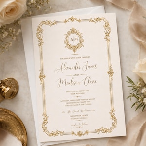 Peut inclure: Une carte d'invitation de mariage couleur crème avec une bordure dorée ornée et un monogramme central avec les lettres A et M. Le texte indique les noms Alexander James et Madison Claire, ainsi que la date et le lieu de la cérémonie.