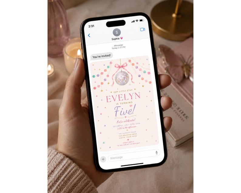 May include: A smartphone displaying a digital birthday invitation on its screen. The invitation features a light pink background with a disco ball, colorful bunting, and text that reads: Our little star Evelyn is turning Five! Let's celebrate.