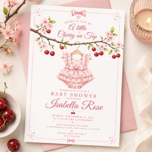 May include: A rectangular baby shower invitation card featuring a pink ruffled baby romper hanging from a cherry blossom branch with red cherries. The text reads: Sweet as can be A little Cherry on Top, Baby Shower honouring Isabella Rose, Sunday, September 14, 2025 at 1:30 in the afternoon, Pink Blossom Tea Room, 23 Bloomfield Lane, San Diego, CA 92128, Kindly RSVP to Emily 619.555.2949.