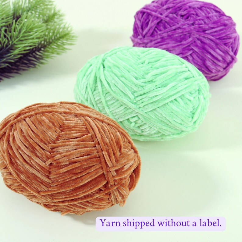 May include: Three balls of soft yarn in shades of brown, mint green, and purple. The yarn is arranged in a row, with the brown ball in the foreground. The text "Yarn shipped without a label" is at the bottom.