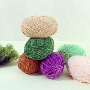 May include: A collection of colorful yarn balls in shades of beige, green, orange, purple, and pink. The yarn balls are arranged in a stack and scattered around, showcasing their soft texture and vibrant colors. Ideal for knitting and crochet projects.