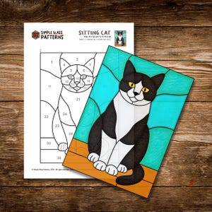 K&ouml;nnte beinhalten: Ein Glasmalereimuster und ein fertiges St&uuml;ck mit einer sitzenden Katze. Das Muster ist schwarz und wei&szlig; mit nummerierten Abschnitten. Das fertige St&uuml;ck zeigt eine schwarz-wei&szlig;e Katze mit gelben Augen vor blauem Hintergrund. Der Text "SITTING CAT" ist sichtbar.