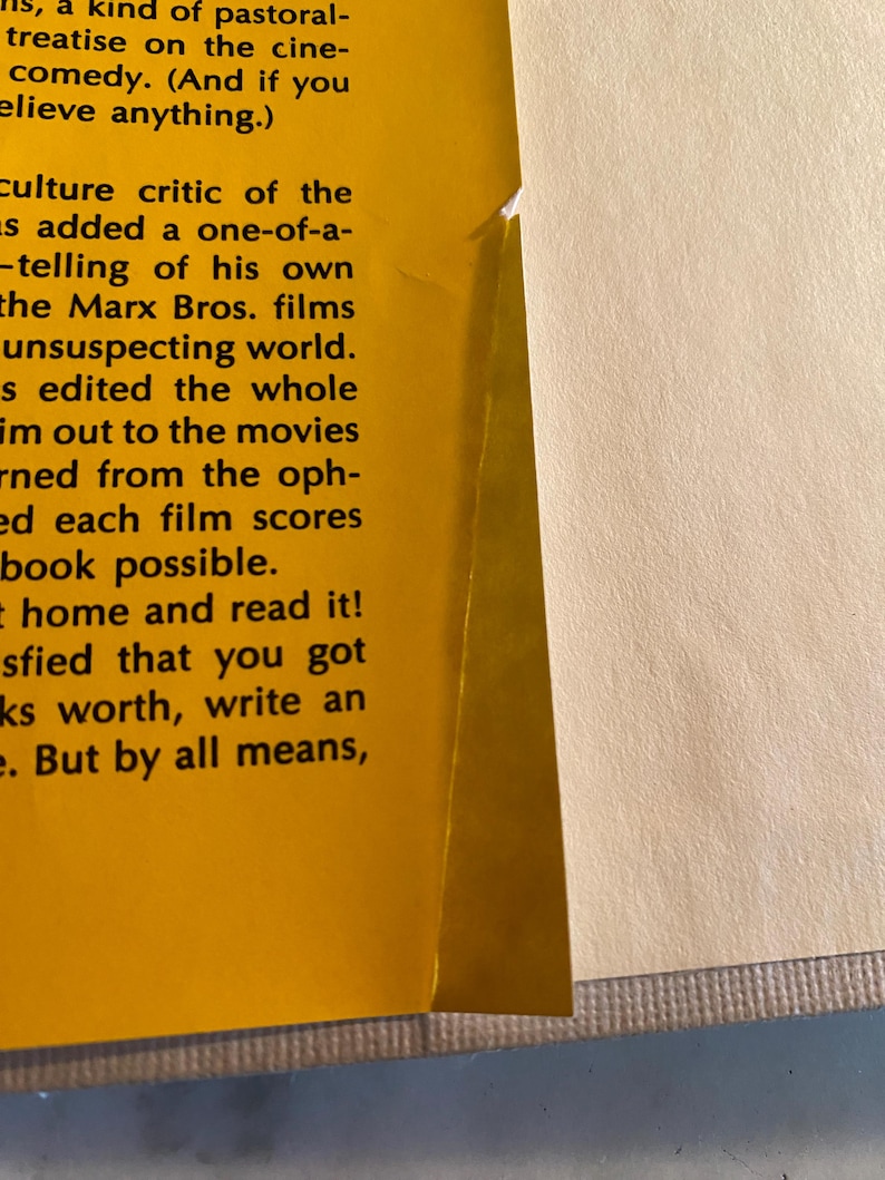 以下が含まれることがあります： 本のページのクローズアップ。左ページは黄色で、"pastoral treatise"や"Marx Bros. films"などの黒いテキストが含まれています。右ページはオフホワイトです。本の端が見えます。