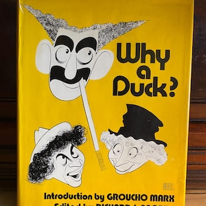 以下が含まれることがあります： 鮮やかな黄色の背景に、太字の黒い文字で「Why a Duck?」と書かれたヴィンテージ本の表紙。表紙には、グルーチョ・マルクスなどの漫画イラストが描かれています。本の序文はグルーチョ・マルクスによるものです。