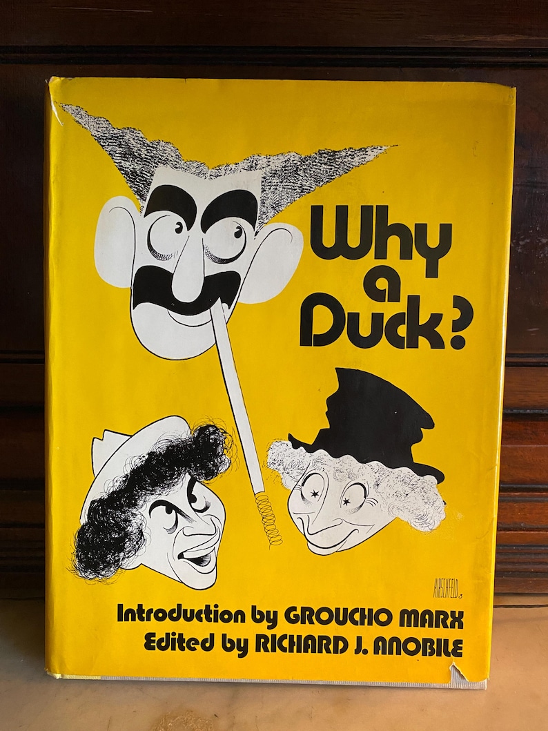 以下が含まれることがあります： 鮮やかな黄色の背景に、太字の黒い文字で「Why a Duck?」と書かれたヴィンテージ本の表紙。表紙には、グルーチョ・マルクスなどの漫画イラストが描かれています。本の序文はグルーチョ・マルクスによるものです。