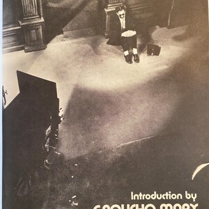 以下が含まれることがあります： グルーチョ・マルクスがスーツとサングラス姿で床に座っている白黒写真。テキスト「Introduction by GROUCHO MARX」が含まれています。