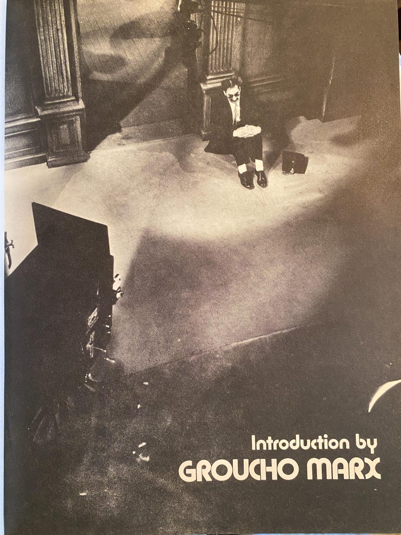 以下が含まれることがあります： グルーチョ・マルクスがスーツとサングラス姿で床に座っている白黒写真。テキスト「Introduction by GROUCHO MARX」が含まれています。