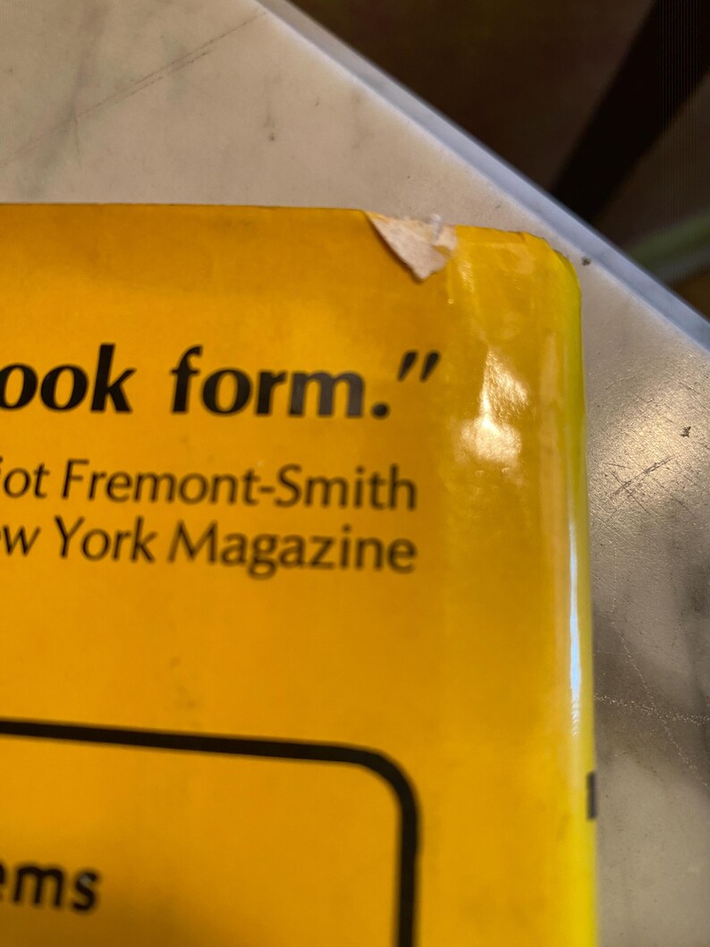 以下が含まれることがあります： 「ook form.」のテキストと「Fremont-Smith」と「New York Magazine」の名前が書かれた、本の黄色の表紙のクローズアップ。 本の右上隅が少し破損しています。