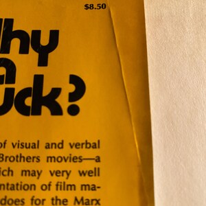 以下が含まれることがあります： 黄色い背景に「Why a Duck?」というタイトルが大きな黒い文字で書かれた本の表紙の一部。右上には8.50ドルの価格が表示されています。表紙には、マルクス兄弟の映画に関するテキストも含まれています。