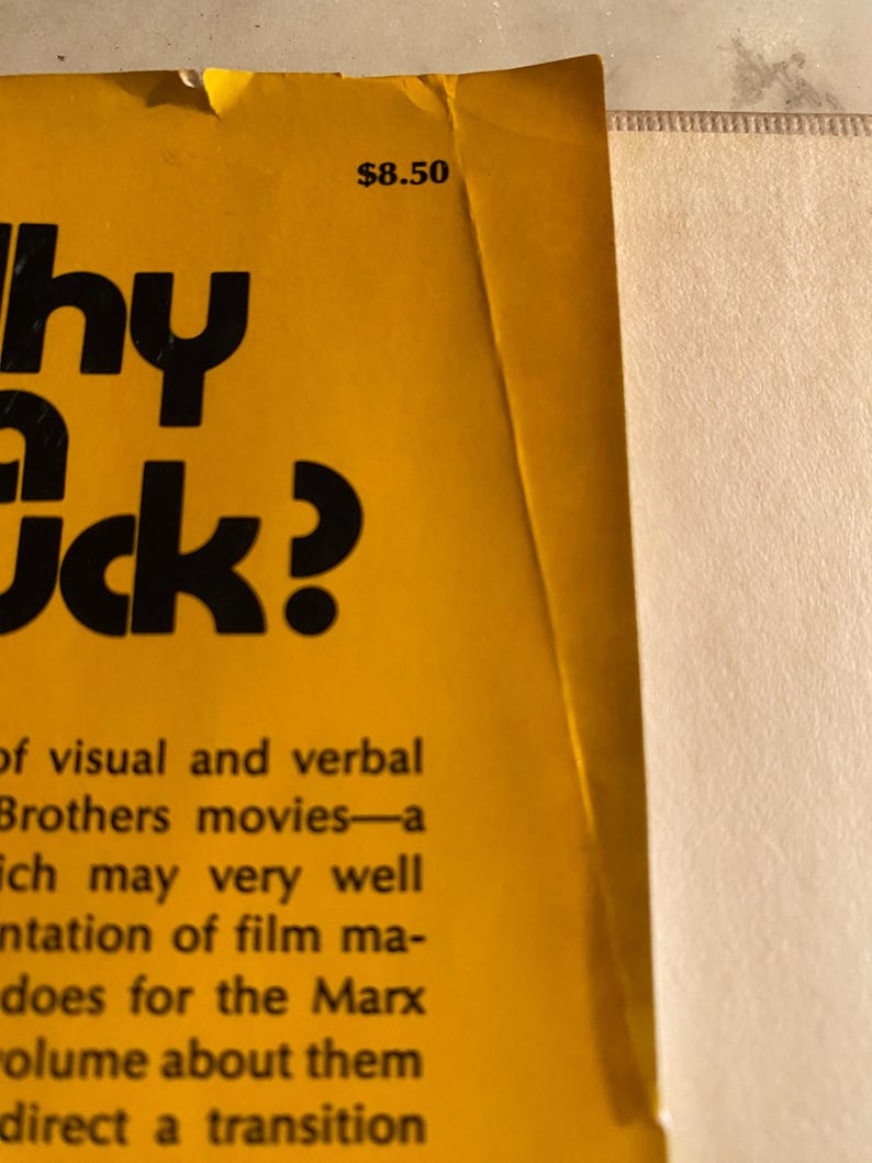 以下が含まれることがあります： 黄色い背景に「Why a Duck?」というタイトルが大きな黒い文字で書かれた本の表紙の一部。右上には8.50ドルの価格が表示されています。表紙には、マルクス兄弟の映画に関するテキストも含まれています。