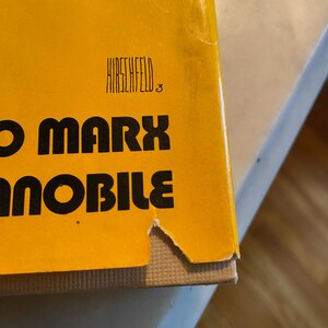 以下が含まれることがあります： 大きな黒い文字で「O Marx」というタイトルが書かれた本の表紙のクローズアップ。表紙は黄色で、タイトルの上に「HIRSCHFELD」という名前が印刷されています。本の角が少し破損しています。