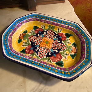 May include: A rectangular ceramic serving dish with rounded corners, featuring a vibrant yellow center decorated with red, orange, and green floral patterns. The wide rim is painted with blue, purple, and green geometric and floral motifs.