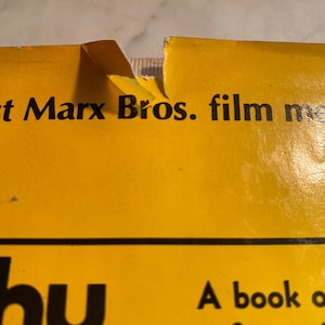 以下が含まれることがあります： 端が破れた本の表紙のクローズアップ。表紙は黄色で、黒い文字で「t Marx Bros. film me」と「hy」と書かれています。この本は伝記のようです。
