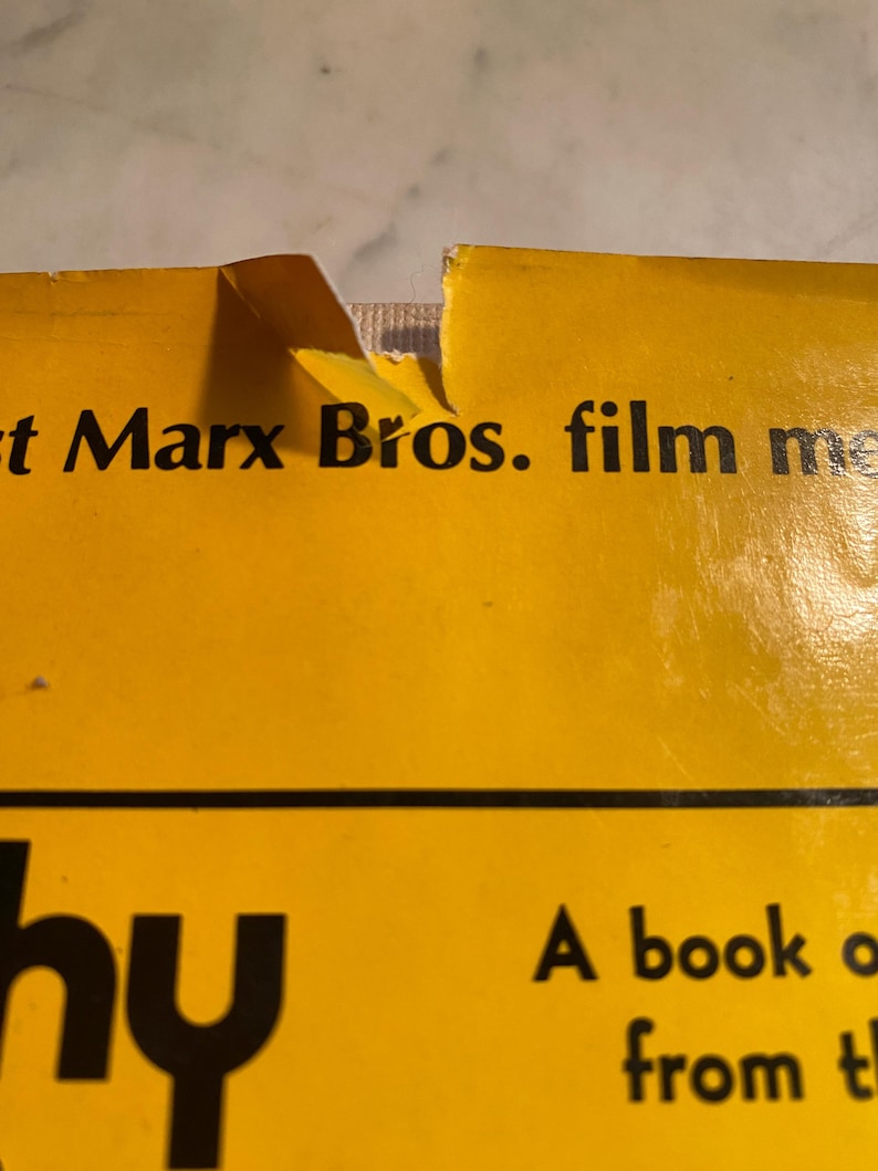 以下が含まれることがあります： 端が破れた本の表紙のクローズアップ。表紙は黄色で、黒い文字で「t Marx Bros. film me」と「hy」と書かれています。この本は伝記のようです。