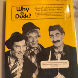 以下が含まれることがあります： 「Why Duck?」のタイトルとマルクス兄弟の写真が描かれた黄色の本の表紙。表紙には、映画の記念碑であり、マルクス兄弟の映画からの言葉とビジュアルゲームであることについてのテキストが含まれています。