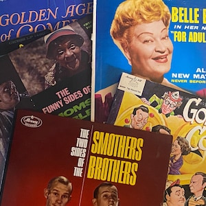 May include: A collection of vintage comedy record albums. The albums feature colorful cover art with images of comedians and the titles "The Golden Age of Comedy", "The Funny Sides of Toms Lef", and "The Smothers Brothers". One album features Belle Barth.