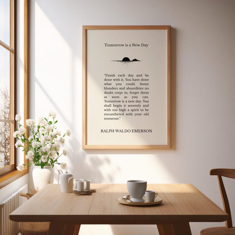 May include: A framed print with the text "Tomorrow is a New Day" and a quote by Ralph Waldo Emerson. The print is in a wooden frame and is displayed on a table with a vase of white flowers and a tea set.