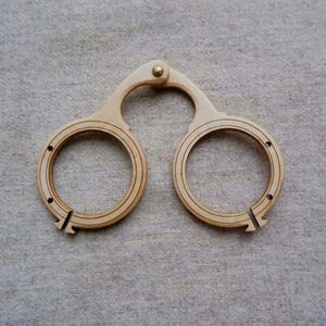 Può includere: Uno strumento in legno chiaro con due componenti circolari collegati da un manico curvo. I cerchi hanno scanalature concentriche e sono uniti con un rivetto color ottone. Lo strumento sembra essere in legno.