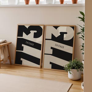 Puede incluir: Dos láminas enmarcadas con un diseño gráfico en blanco y negro con el número 73 y la palabra "Chicago". Las láminas se exhiben sobre un suelo de madera, apoyadas en una pared. También hay un pequeño taburete de madera y plantas en la habitación.
