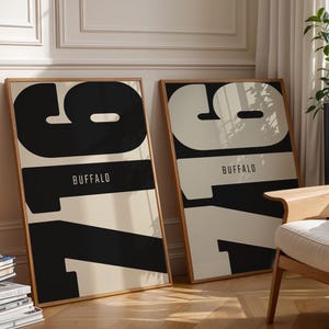Op de afbeelding: Twee rechthoekige ingelijste wandposters met het getal 716 in grote, dikke typografie en het woord BUFFALO in kleinere letters eronder. De ene print heeft zwarte cijfers op een crèmekleurige achtergrond, de andere crèmekleurige cijfers op zwart.
