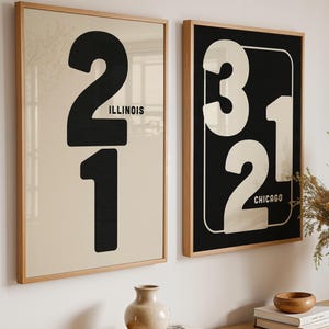 Puede incluir: Dos láminas enmarcadas con números grandes y texto. Una lámina presenta el número "21" con "ILLINOIS" debajo, sobre un fondo beige. La otra lámina tiene "312" con "CHICAGO" sobre un fondo negro. Ambas están en marcos de madera.