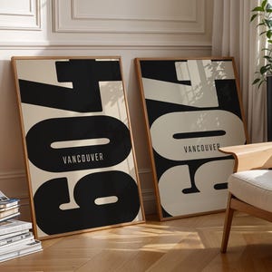 Può includere: Due stampe artistiche incorniciate con la parola "Vancouver" e il numero "604" in bianco e nero. Le stampe sono esposte in una stanza luminosa con pavimento in legno e una sedia moderna.
