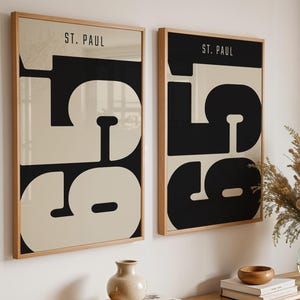 Peut inclure: Deux affiches murales rectangulaires dans des cadres en bois clair, chacune présentant le texte ST. PAUL et les grands chiffres noirs 551 sur un fond crème. Les affiches sont exposées côte à côte, avec un design graphique aux lignes épurées.