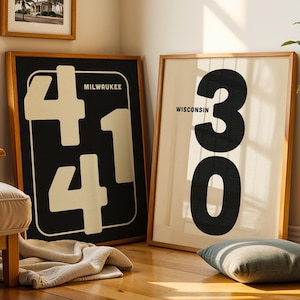 May include: Two framed art prints with wooden frames. One shows the number "41" in white on a black background, with "MILWAUKEE" above. The other displays the number "30" in black on a cream background, with "WISCONSIN" above.