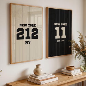 Puede incluir: Dos cuadros enmarcados con temática deportiva. Uno muestra "NEW YORK 212 NY" en negro sobre fondo crema, el otro "NEW YORK 11 EST. 1788" en blanco sobre negro. Ambos en marcos de madera.