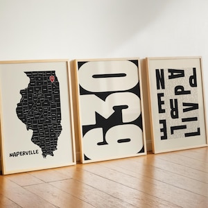 May include: Three framed wall art prints in light wood frames. The first shows a black map of Illinois with a red location pin over Naperville. The second features the large black numbers 630. The third displays the word NAPERVILLE in black text.