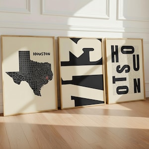 May include: Three framed wall art prints with light cream backgrounds and black graphics. The first shows a map of Texas with a red location pin on Houston. The second features the large black numbers 713. The third displays the word HOUSTON.
