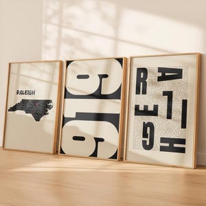May include: Three framed wall art prints in light wood frames. The first shows a black map of North Carolina with a red location pin and the text RALEIGH. The second features large black numbers 919. The third displays the word RALEIGH in bold black letters.