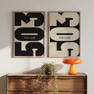 Peut inclure: Deux affiches murales rectangulaires encadrées présentant les grands chiffres 503 en noir et beige avec le mot PORTLAND imprimé au centre. L'affiche de gauche a des chiffres noirs sur fond beige, et celle de droite a des chiffres beiges sur fond noir.