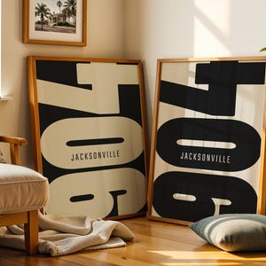 May include: Two framed art prints with a minimalist design. Each print features the number "706" in large black block letters against a cream background, with "JACKSONVILLE" printed below. The frames are light wood.