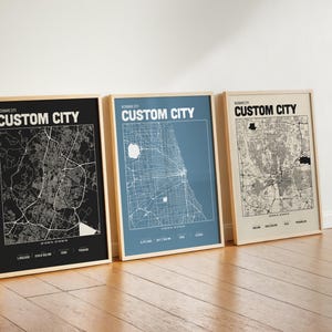 Peut inclure: Trois affiches verticales encadrées présentant des plans de ville personnalisés. L'affiche de gauche est noire avec des lignes blanches, celle du centre est bleue avec des lignes blanches, et celle de droite est beige avec des lignes noires.