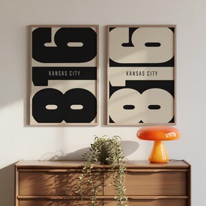 May include: Two framed rectangular wall art prints featuring the large black and cream numbers 816 with the text KANSAS CITY centered horizontally. The left print has a black background with cream numbers, while the right print has a cream background with black numbers.