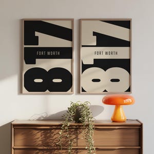 Könnte beinhalten: Zwei gerahmte Kunstdrucke mit dem Text "FORT WORTH" und der Zahl "18" in einem kräftigen, modernen Design. Die Drucke sind in Schwarz und Creme gehalten. Die Drucke werden über einer Holzkommode ausgestellt.