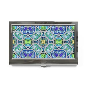 May include: A silver business card holder with a colorful, intricate stained-glass pattern. The design features a repeating pattern of blue, green, and yellow floral and geometric shapes, creating a vibrant and artistic appearance. The holder has a rectangular shape with a hinged opening.