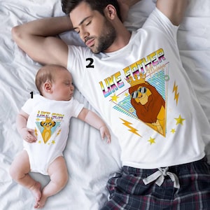 May include: White t-shirts and a baby onesie with matching graphics. The shirts feature a lion wearing sunglasses and a crown, with the text "LIKE FATHER" and "LIKE SON". The design includes stars and lightning bolts.