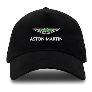 May include: Black baseball cap featuring the Aston Martin logo. The logo is a stylized wing design with green and white accents, and the brand name is printed in white below the logo. The cap is a classic, curved-brim style.