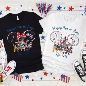 以下が含まれることがあります： 7月4日の愛国的なデザインの黒と白のTシャツ。花火、テキスト「Happy 4th of July」、年号「Est. 1776」が特徴のディズニーをテーマにしたグラフィックがプリントされています。