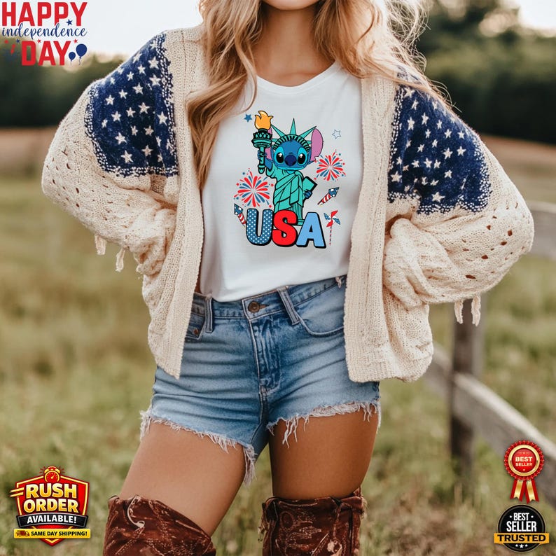 Puede incluir: Camiseta blanca con un gr&aacute;fico de Stitch como la Estatua de la Libertad sosteniendo una antorcha, con la palabra "USA" en rojo, blanco y azul. La camiseta se usa con pantalones cortos de mezclilla y una rebeca color crema con mangas con estampado de estrellas azules. La imagen incluye el texto "Happy Independence Day".
