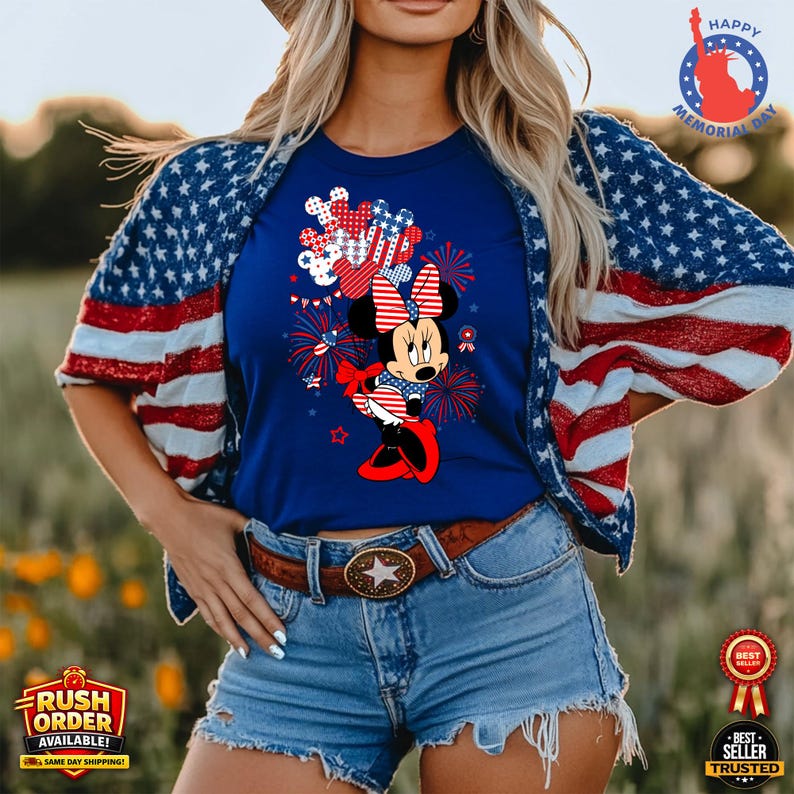 Puede incluir: Una camiseta azul marino con Minnie Mouse en un dise&ntilde;o patri&oacute;tico con acentos rojos, blancos y azules. El atuendo incluye pantalones cortos de mezclilla y una chaqueta con un patr&oacute;n de bandera estadounidense. Un cintur&oacute;n marr&oacute;n con hebilla de estrella completa el look. Tambi&eacute;n aparece el texto "Happy Memorial Day".
