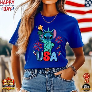 Puede incluir: Camiseta azul con un personaje de dibujos animados como la Estatua de la Libertad sosteniendo una antorcha, con la palabra "USA" en colores patri&oacute;ticos. Fuegos artificiales y estrellas rodean el dise&ntilde;o. La camiseta tambi&eacute;n tiene el texto "Happy Independence Day".