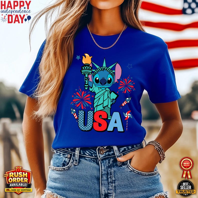 Puede incluir: Camiseta azul con un personaje de dibujos animados como la Estatua de la Libertad sosteniendo una antorcha, con la palabra "USA" en colores patri&oacute;ticos. Fuegos artificiales y estrellas rodean el dise&ntilde;o. La camiseta tambi&eacute;n tiene el texto "Happy Independence Day".
