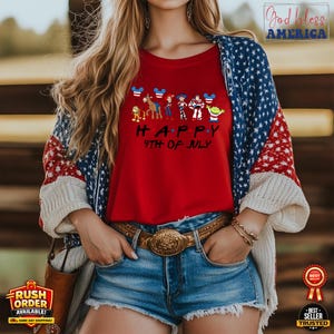 Puede incluir: Una camiseta roja con el texto "HAPPY 4TH OF JULY" y personajes de dibujos animados. La persona lleva unos pantalones cortos vaqueros azules, un cintur&oacute;n marr&oacute;n con hebilla dorada y una rebeca con estampado rojo, blanco y azul.