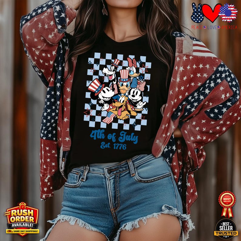 Puede incluir: Camiseta negra con un dise&ntilde;o de personajes de Disney celebrando el 4 de julio. El dise&ntilde;o incluye a Mickey Mouse, el Pato Donald y Goofy, sobre un fondo a cuadros. El texto "4th of July Est. 1776" se muestra en azul.