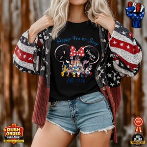 以下が含まれることがあります： 「Happy 4th of July Harper Est. 1776」の文字とディズニーキャラクターのグラフィックがプリントされた黒いTシャツ。赤、白、青のカーディガンとデニムショーツを着用。カーディガンは星とストライプのパターンです。