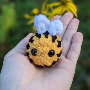 May include: A small crocheted bee toy with black and yellow stripes, white fuzzy wings, and black button eyes.